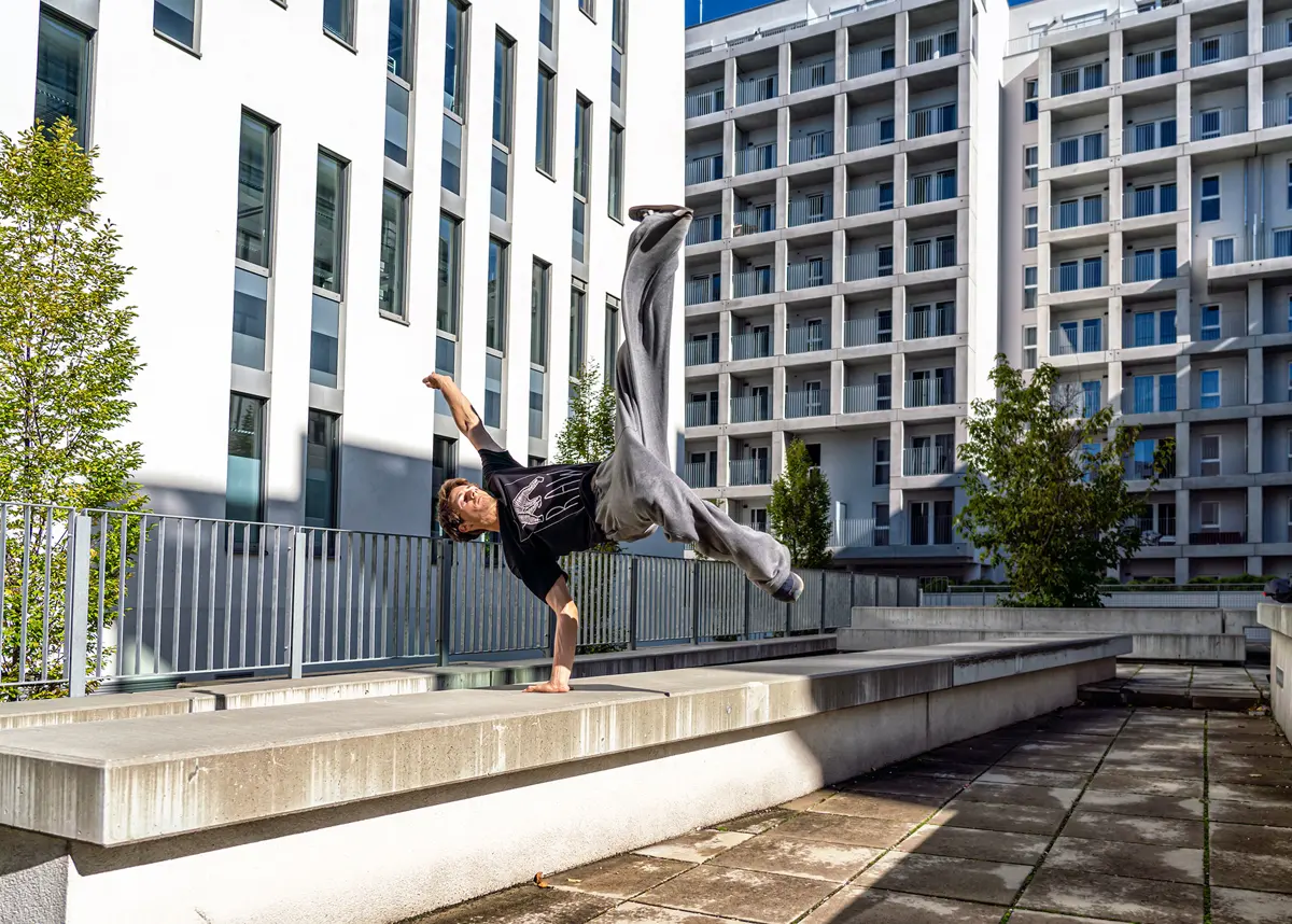 One-arm handstand on a concrete wall between apartment buildings