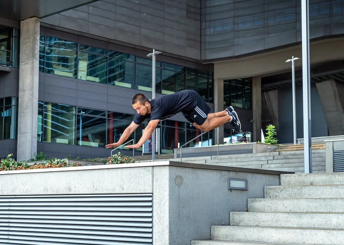 Hands-first parkour vault over a railing in front of concrete steps