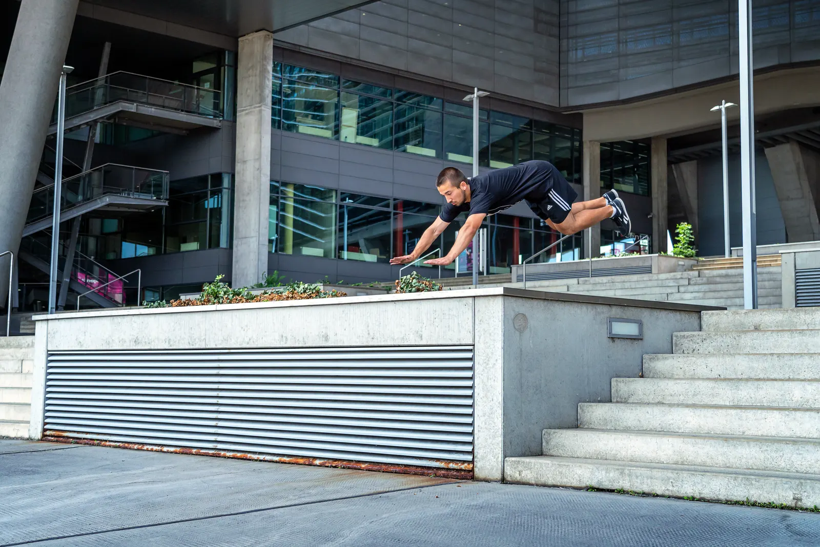 Parkour vault over a railing in front of a modern building with steps